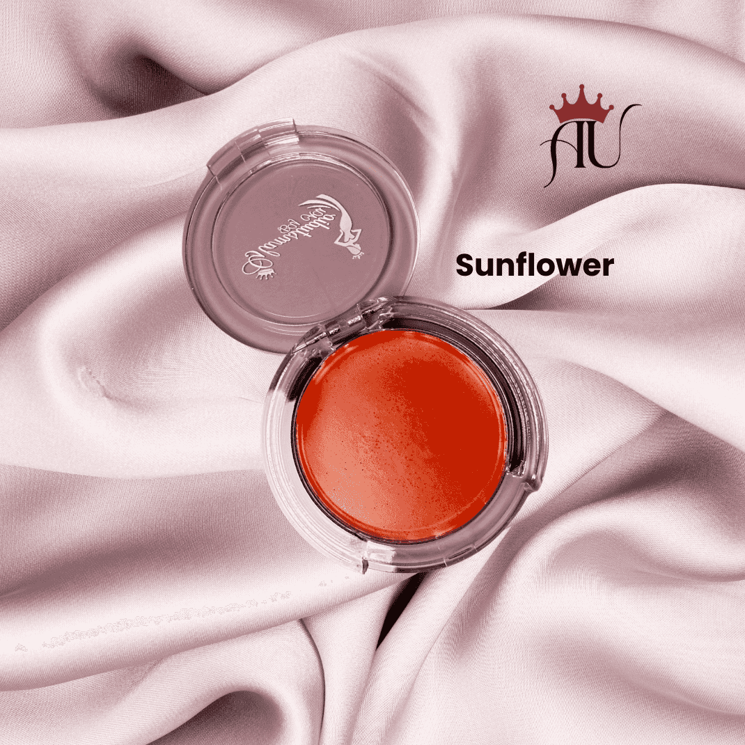 Sunflower Cream Blush in golden-peach tone with creamy, hydrating finish in clear round compact on pink fabric background