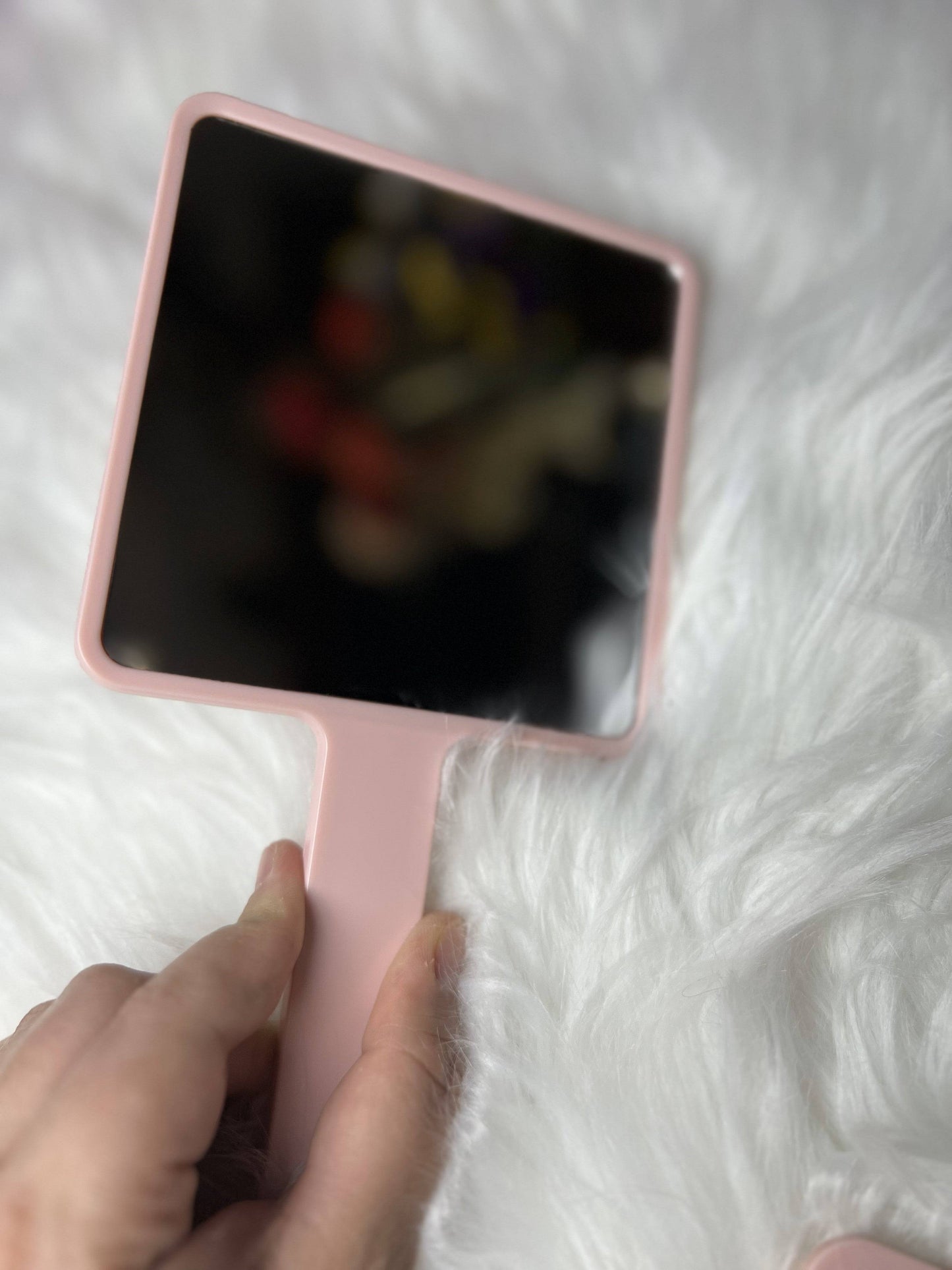 Elegant pink handled mirror with square frame and ergonomic grip for portable makeup and skincare use.